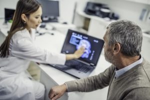 Doctor and patient sitting at desk reviewing patient’s brain scan on laptop