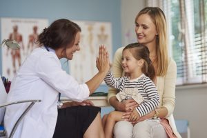 Parent with craniopharyngioma and child in exam room with neurosurgeon giving child high five
